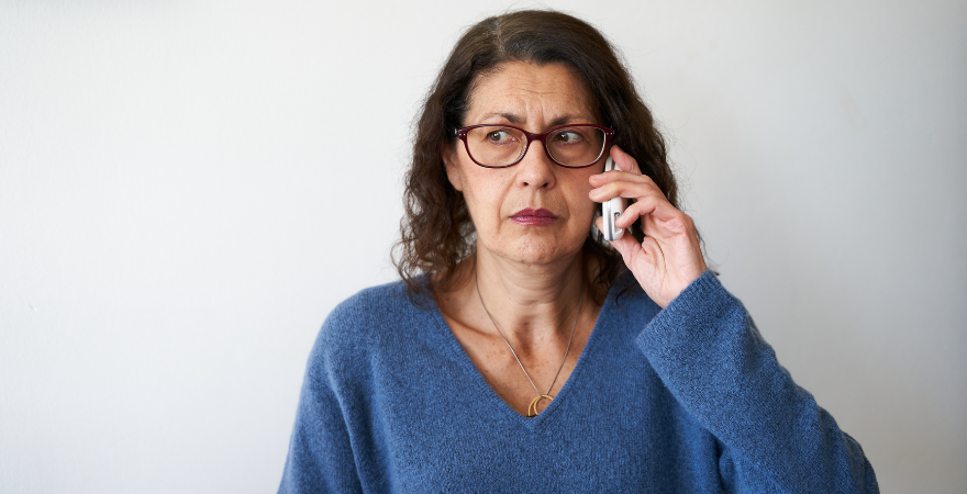 Woman in blue sweater looking concerned while on the phone.