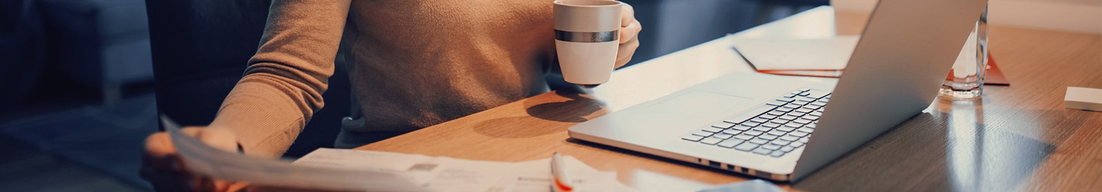 person with coffee cup and laptop open looking at piece of paper