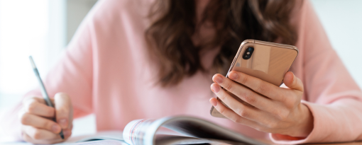 Woman looking at a phone in her hand while writing.