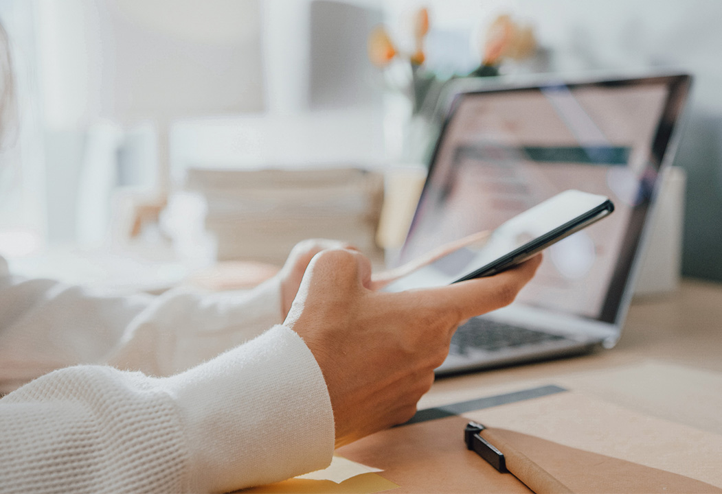 Person holding phone with computer in background