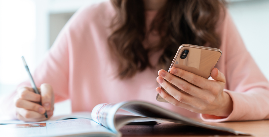 Woman looking at a phone in her hand while writing.