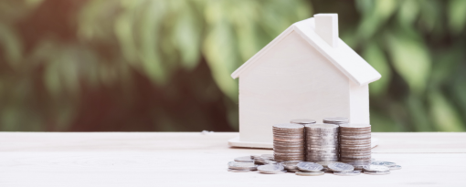 Small white, wooden house with coins stacked in front of it.