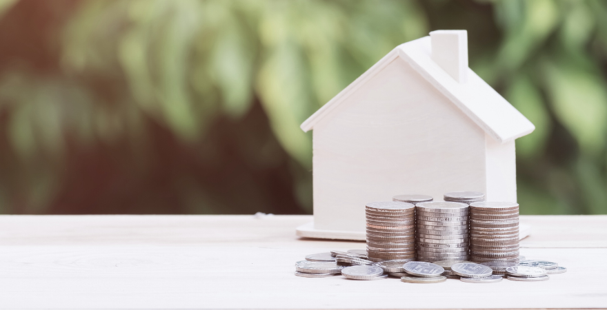 Small white, wooden house with coins stacked in front of it.