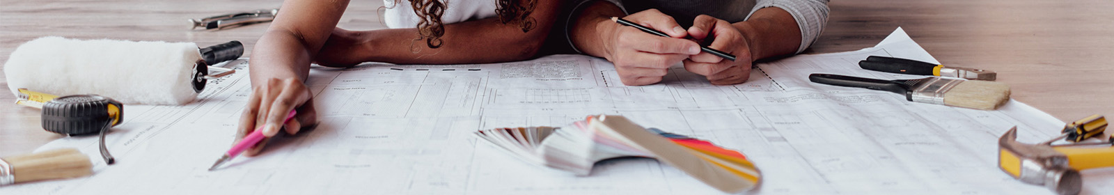 two people looking at building plans with tools scattered around them